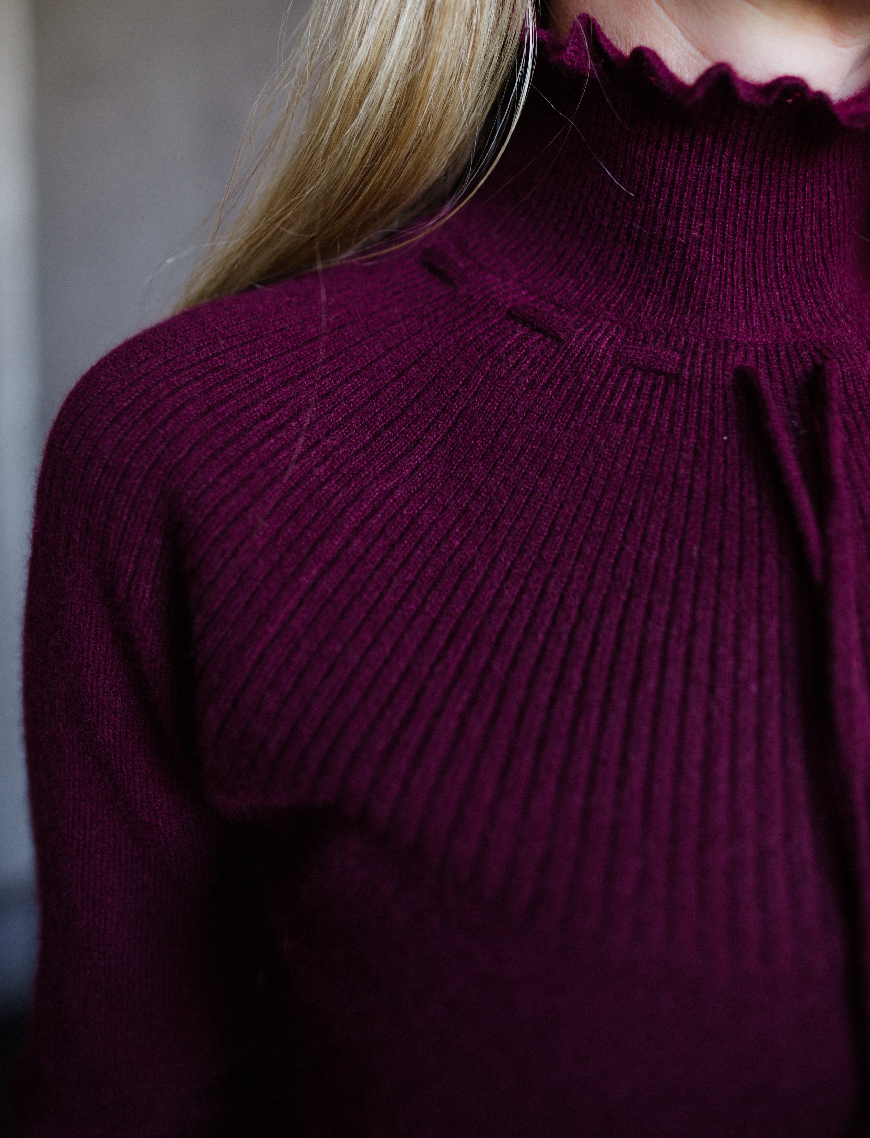 Image featuring a woman wearing the Maisie cashmere sweater by Ulla Johnson with a high neckline, drawstring detailing and a ribbed texture in burgundy.