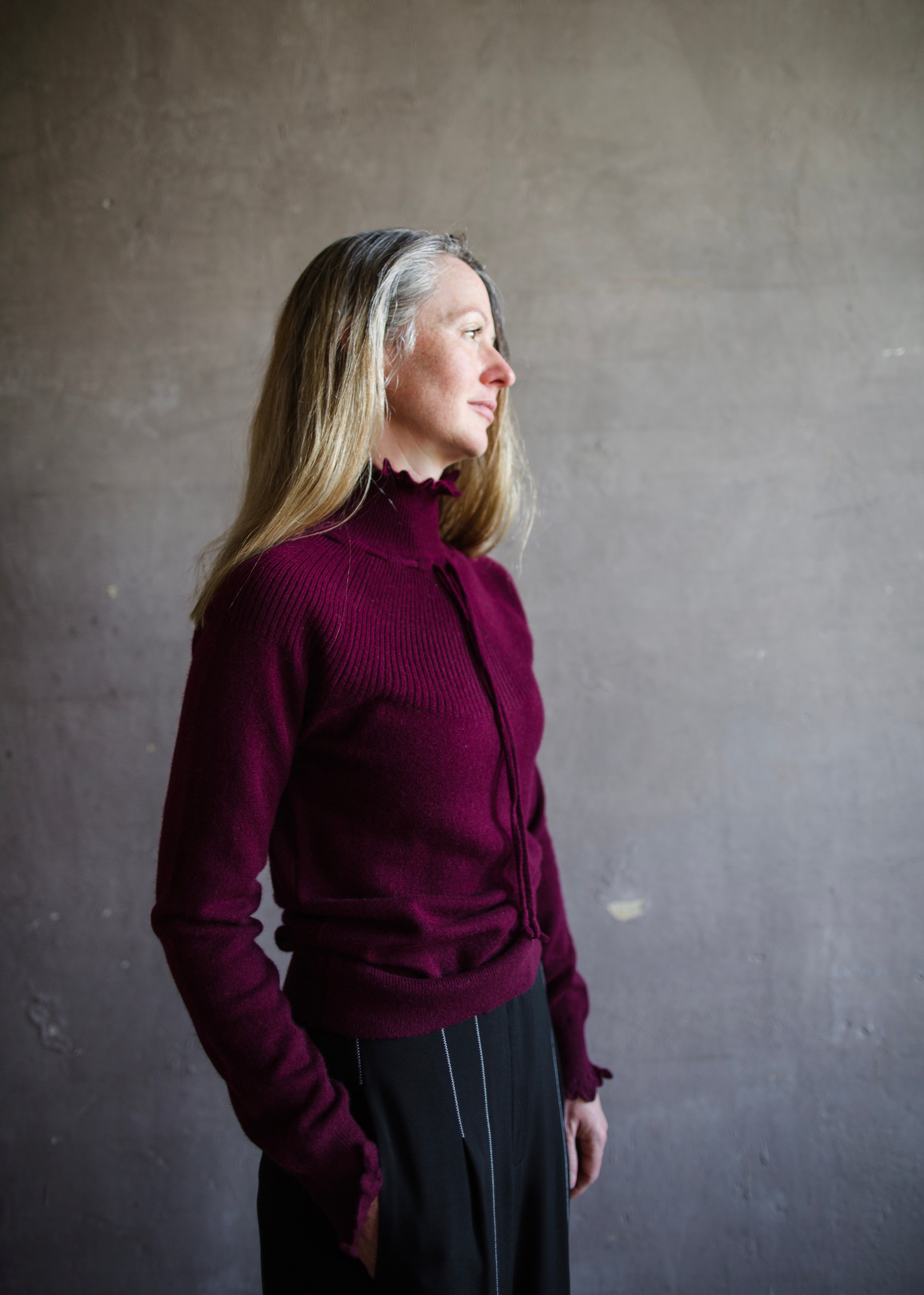 Image featuring a woman wearing the Maisie cashmere sweater by Ulla Johnson with a high neckline, drawstring detailing and a ribbed texture in burgundy.