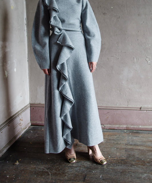 Image featuring a woman wearing he Mireya skirt by Ulla Johnson with a high rise and ruffle trim and a midi fit in soft, textured heather grey wool.