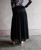 Image featuring a woman wearing the Miya black skirt by Ulla Johnson features a tailored fit though the hips with pleated skirting and a midi hem.