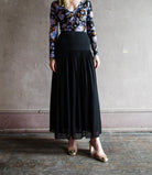 Image featuring a woman wearing the Miya black skirt by Ulla Johnson features a tailored fit though the hips with pleated skirting and a midi hem.