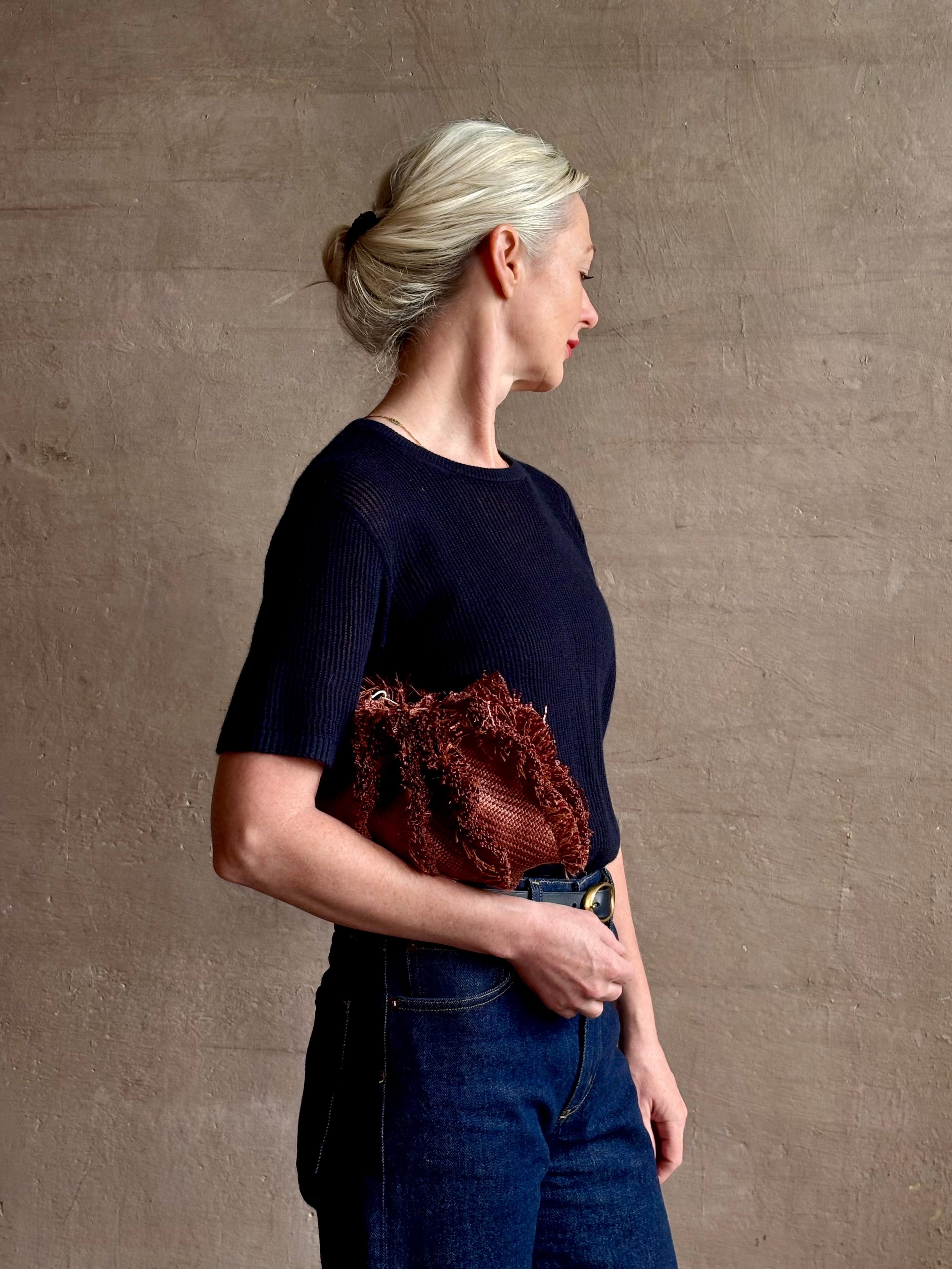 Mature woman with designer Ulla Johnson Adria crossbody bag with raffia-textured exterior and removeable handle that can double as a clutch in a warm brown neutral tone