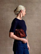 Mature woman with designer Ulla Johnson Adria crossbody bag with raffia-textured exterior and removeable handle that can double as a clutch in a warm brown neutral tone