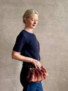 Mature woman with designer Ulla Johnson Adria crossbody bag with raffia-textured exterior and removeable handle that can double as a clutch in a warm brown neutral tone