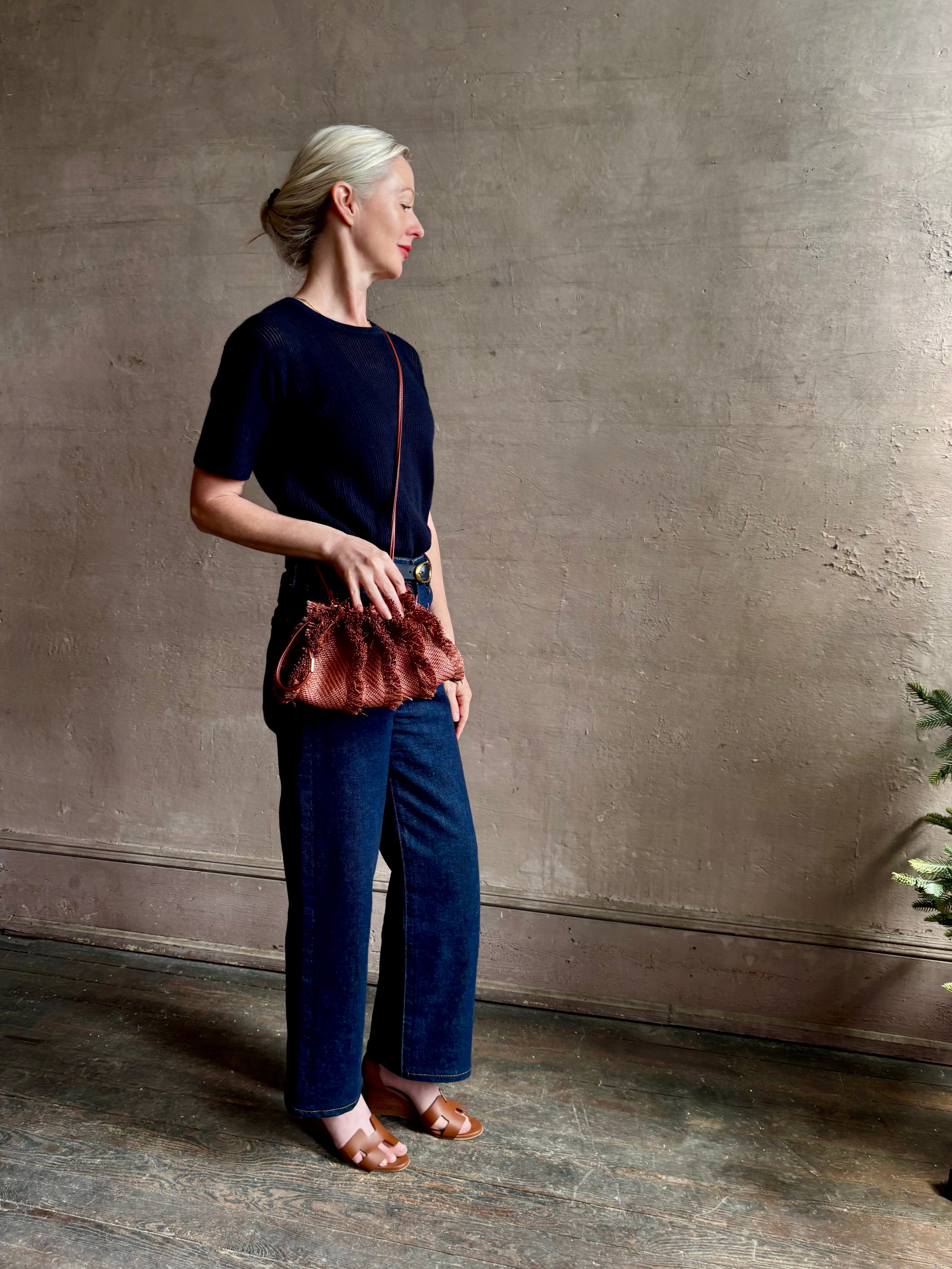 Mature woman with designer Ulla Johnson Adria crossbody bag with raffia-textured exterior and removeable handle that can double as a clutch in a warm brown neutral tone