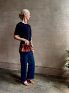 Mature woman with designer Ulla Johnson Adria crossbody bag with raffia-textured exterior and removeable handle that can double as a clutch in a warm brown neutral tone