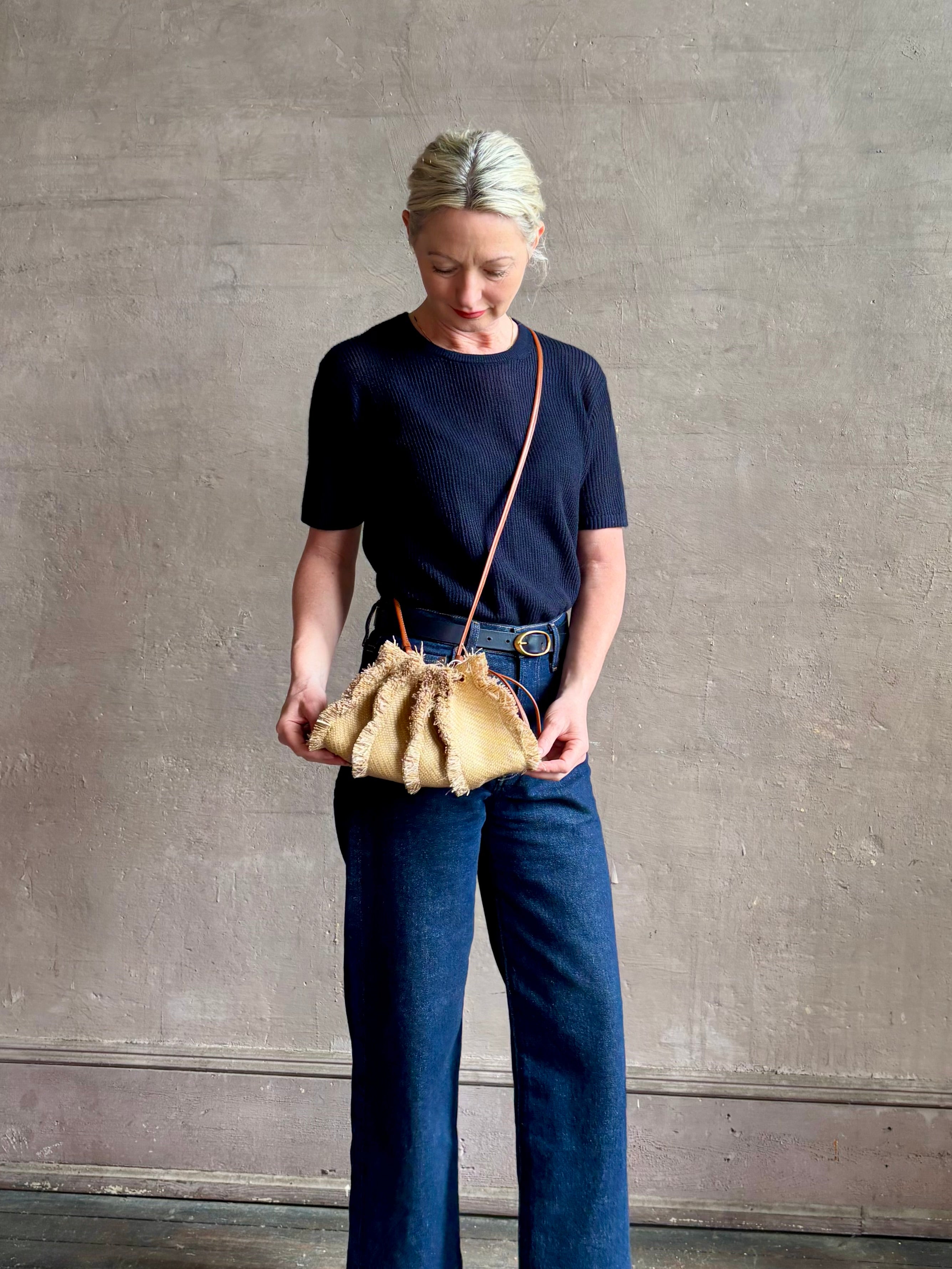 Mature woman with designer Ulla Johnson Adria crossbody bag with raffia-textured exterior and removeable handle that can double as a clutch in a natural raffia tone