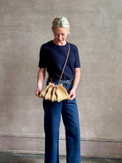 Mature woman with designer Ulla Johnson Adria crossbody bag with raffia-textured exterior and removeable handle that can double as a clutch in a natural raffia tone