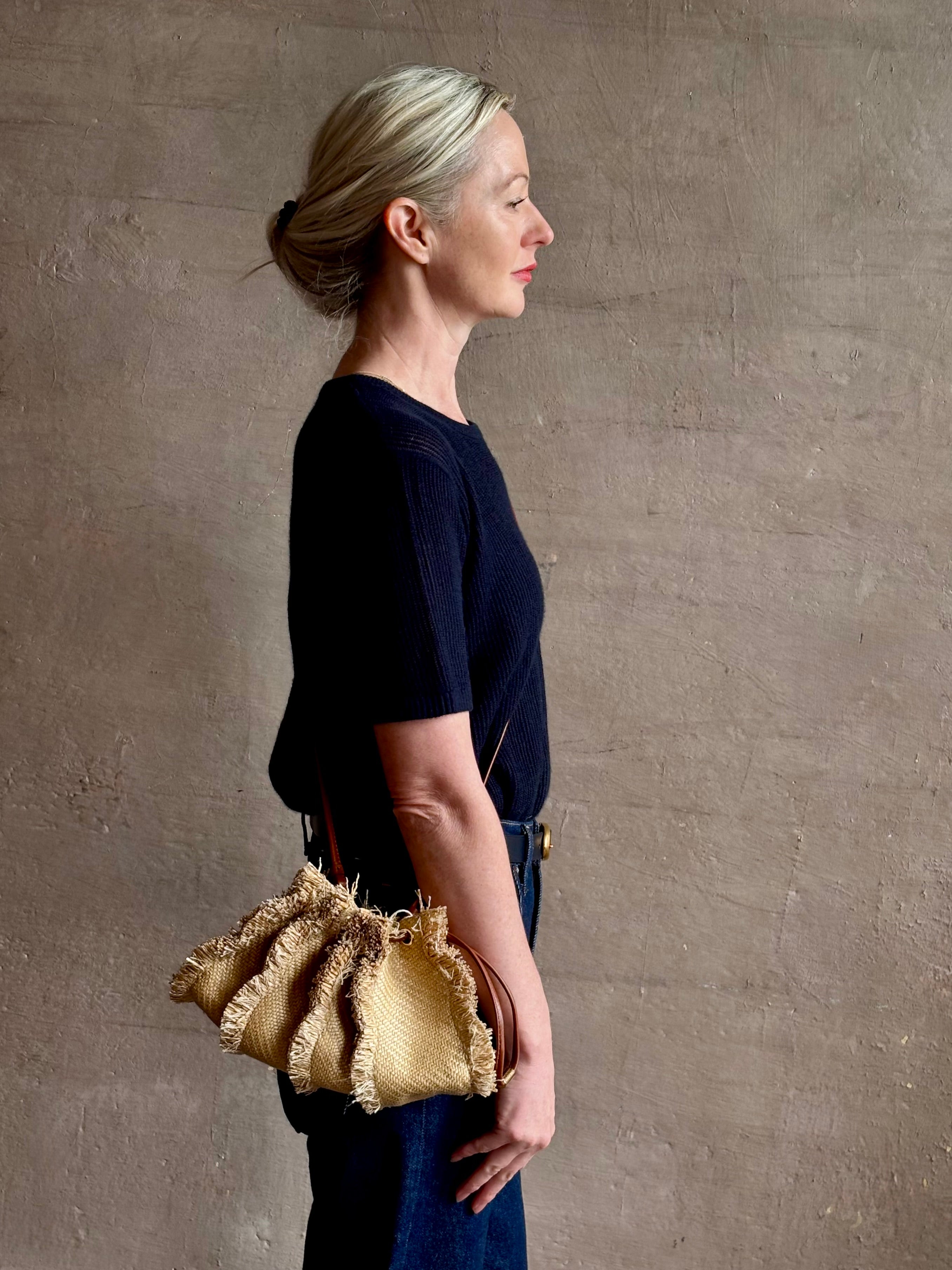 Mature woman with designer Ulla Johnson Adria crossbody bag with raffia-textured exterior and removeable handle that can double as a clutch in a natural raffia tone
