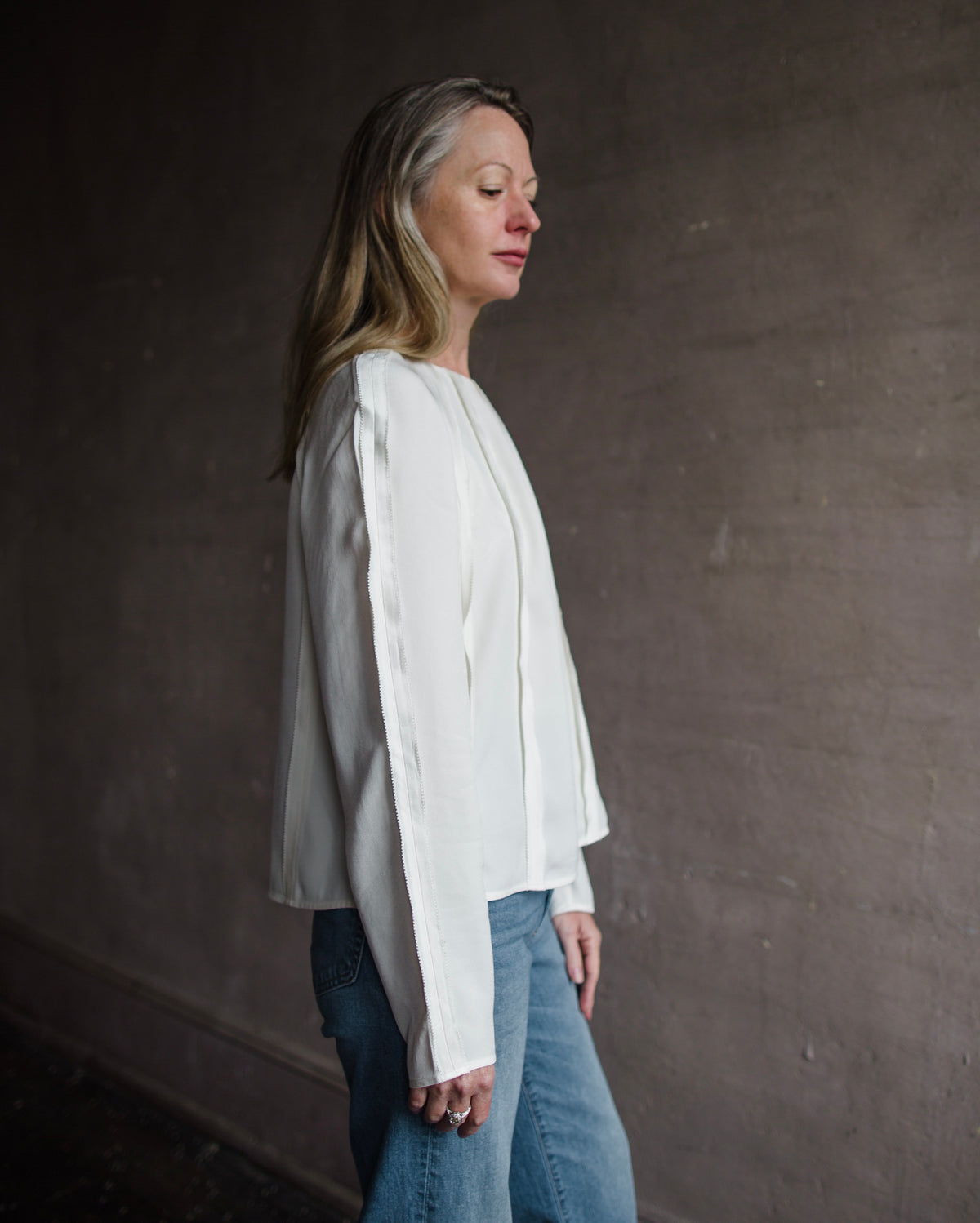 Side profile of mature woman wearing Ulla Johnson Kavi long sleeve Blouse with three dimensional linear seam details crew neck in cream