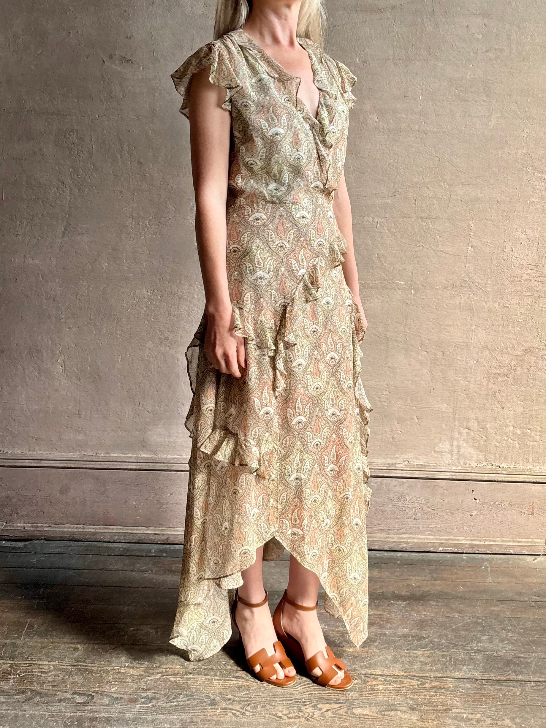 Mature woman wearing the Cap Sleeve Anenel maxi Dress from luxury designer Veronica Beard rendered in a soft khaki, green, and pink paisley print and crafted in silk with cap sleeves, v- neckline, and asymmetrical hem all finished with soft feminine ruffles in a timeless A-line silhouette