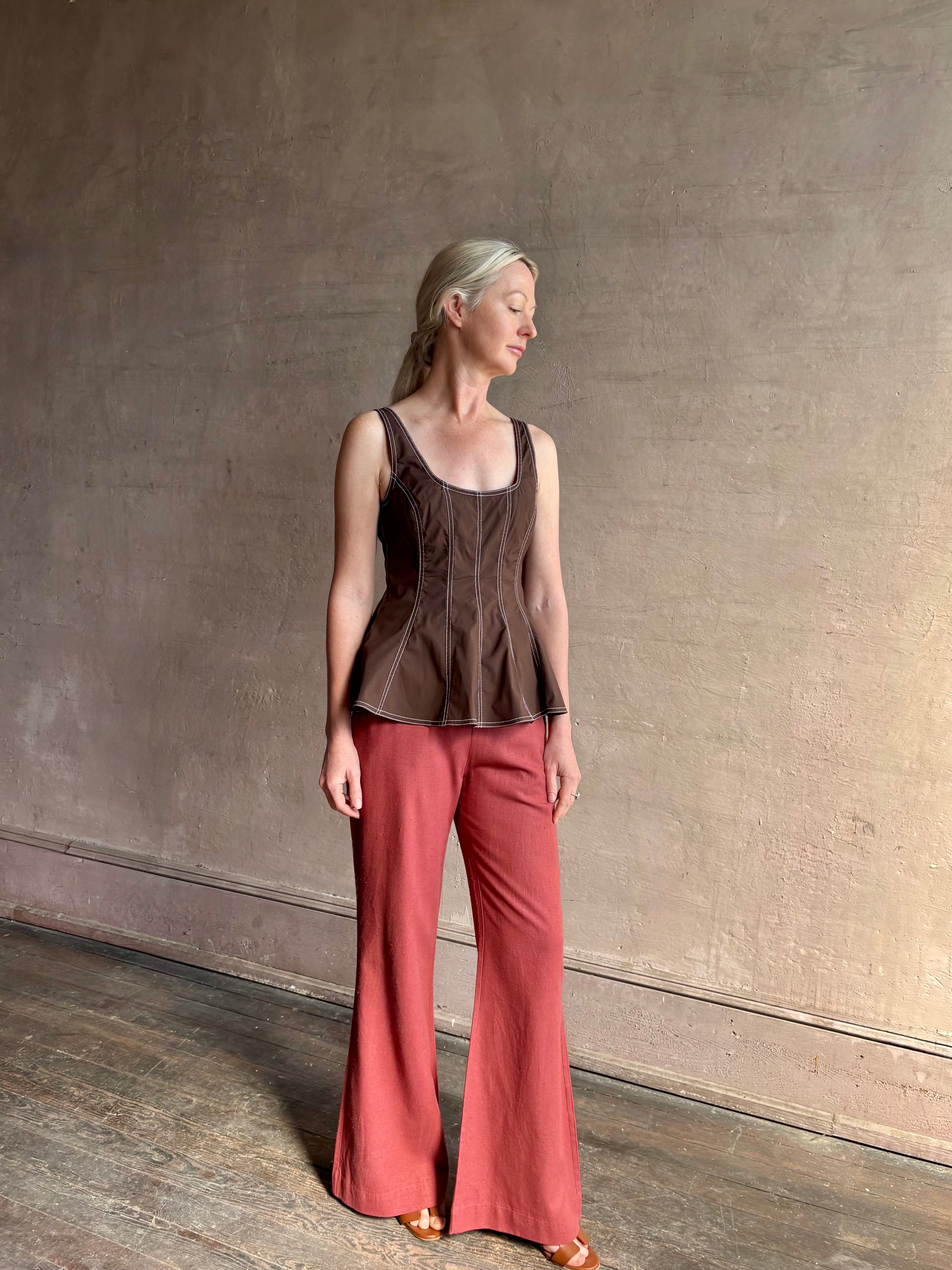 Mature woman wearing the Charlie Top from designer Veronica Beard rendered in dark brown with white contrast stitching and crafted from a cotton blend this peplum offers a flattering silhouette that's sleeveless with a scoop neckline in front and back 