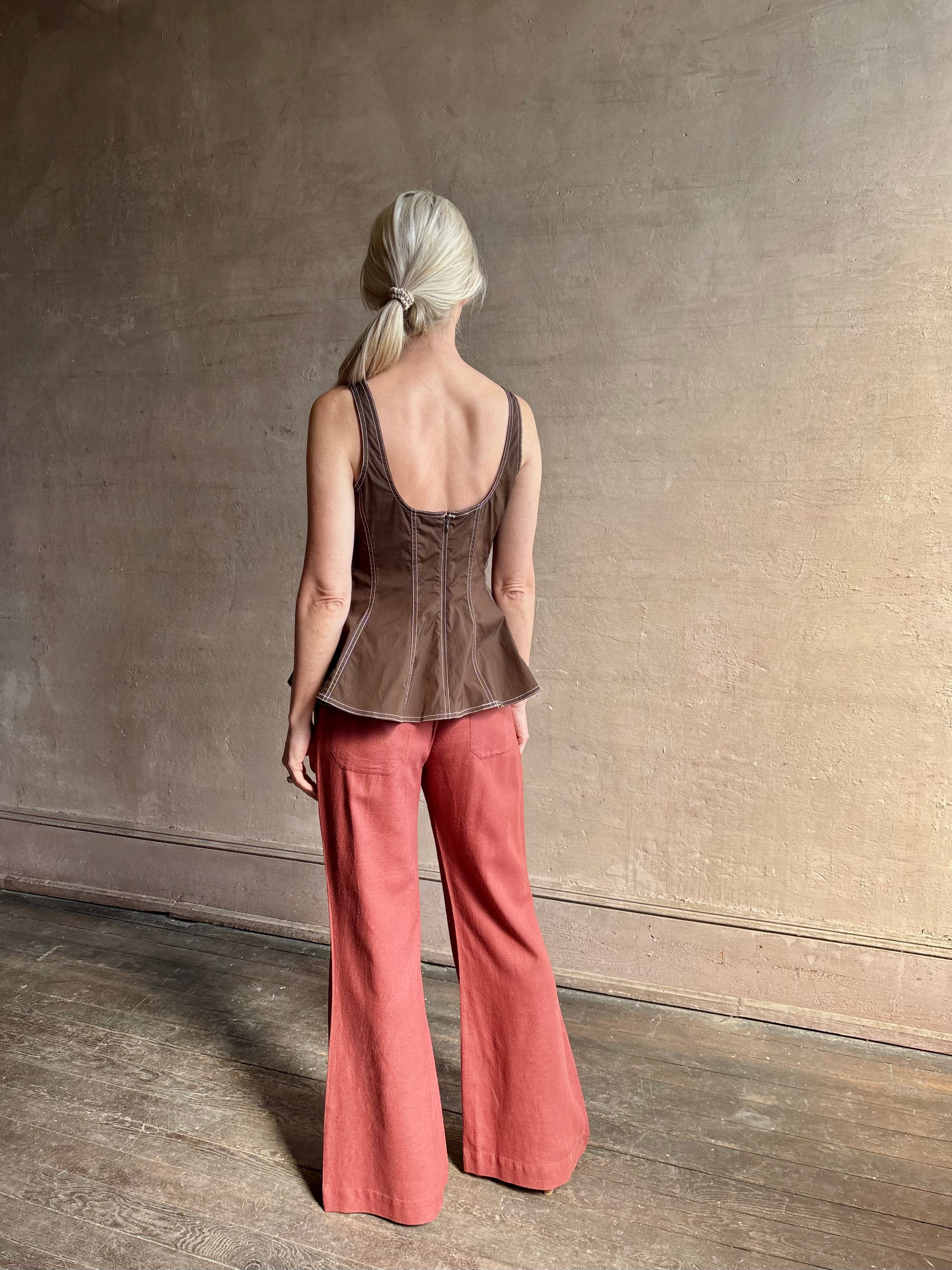 Mature woman wearing the Charlie Top from designer Veronica Beard rendered in dark brown with white contrast stitching and crafted from a cotton blend this peplum offers a flattering silhouette that's sleeveless with a scoop neckline in front and back 