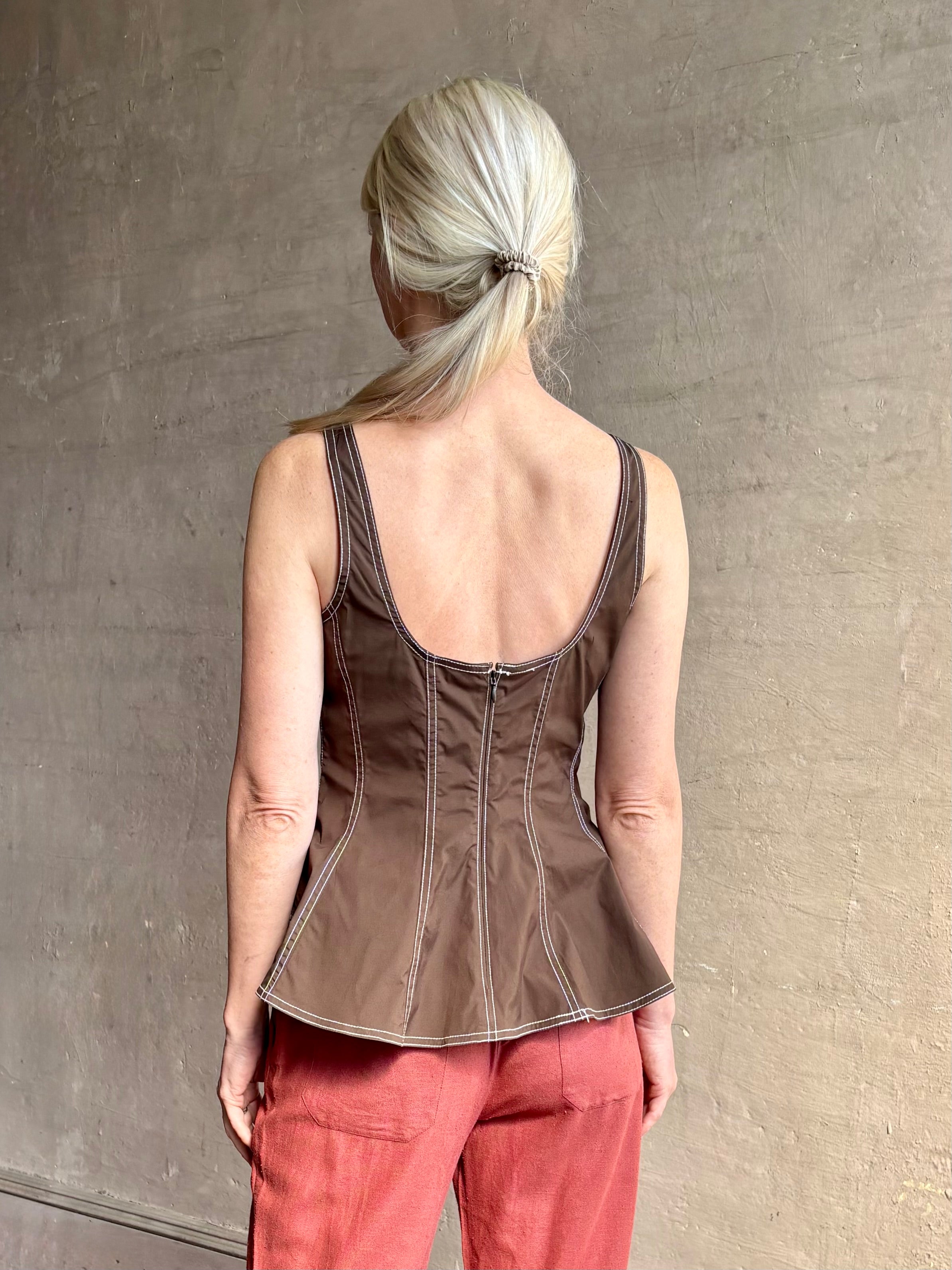 Mature woman wearing the Charlie Top from designer Veronica Beard rendered in dark brown with white contrast stitching and crafted from a cotton blend this peplum offers a flattering silhouette that's sleeveless with a scoop neckline in front and back along with a convenient concealed zip closure