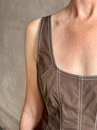 Mature woman wearing the Charlie Top from designer Veronica Beard rendered in dark brown with white contrast stitching and crafted from a cotton blend this peplum offers a flattering silhouette that's sleeveless with a scoop neckline in front and back 