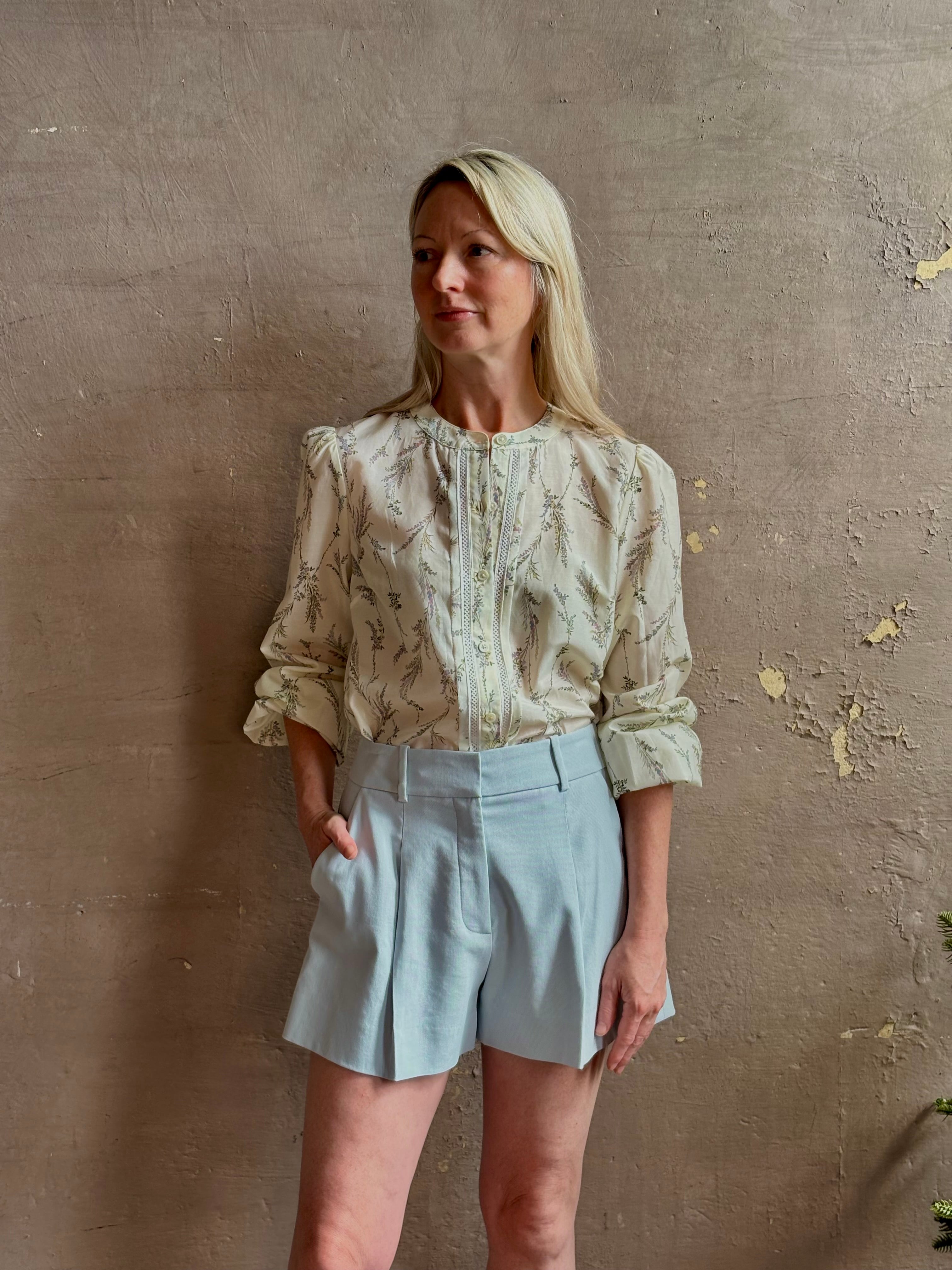 Mature woman wearing elevated Craig Short from Veronica Beard a sophisticated women's designer short rendered in river mist light blue and crafted from a refined blend of cotton and viscose with side pockets, one front pleat and tailored waistband with belt loops