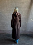 Mature woman wearing Veronica Beard Elspeth Coat with OVS Hoodie Dickey in Espresso brown wool-cashmere A-line coat with a removable hoodie layer. Playful, sculptural cold-weather luxury.