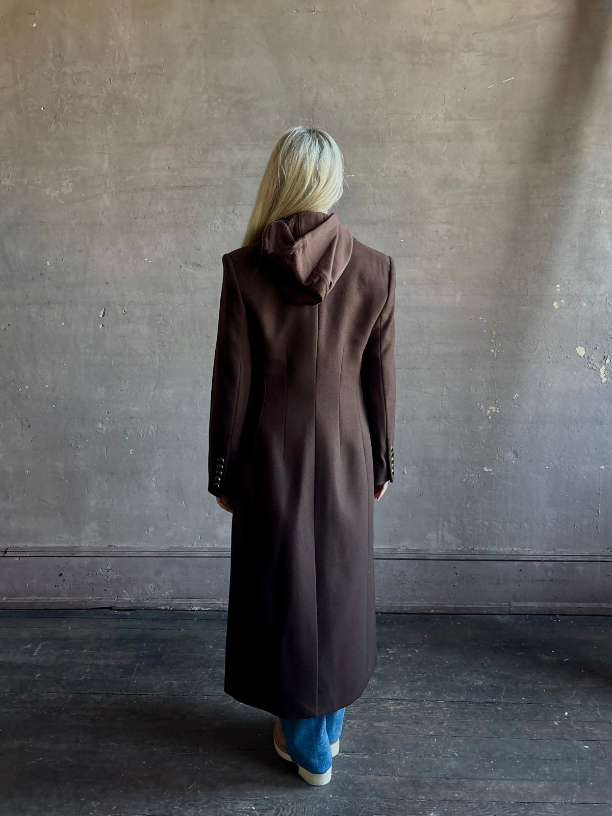 Mature woman wearing Veronica Beard Elspeth Coat with OVS Hoodie Dickey in Espresso brown wool-cashmere A-line coat with a removable hoodie layer. Playful, sculptural cold-weather luxury.