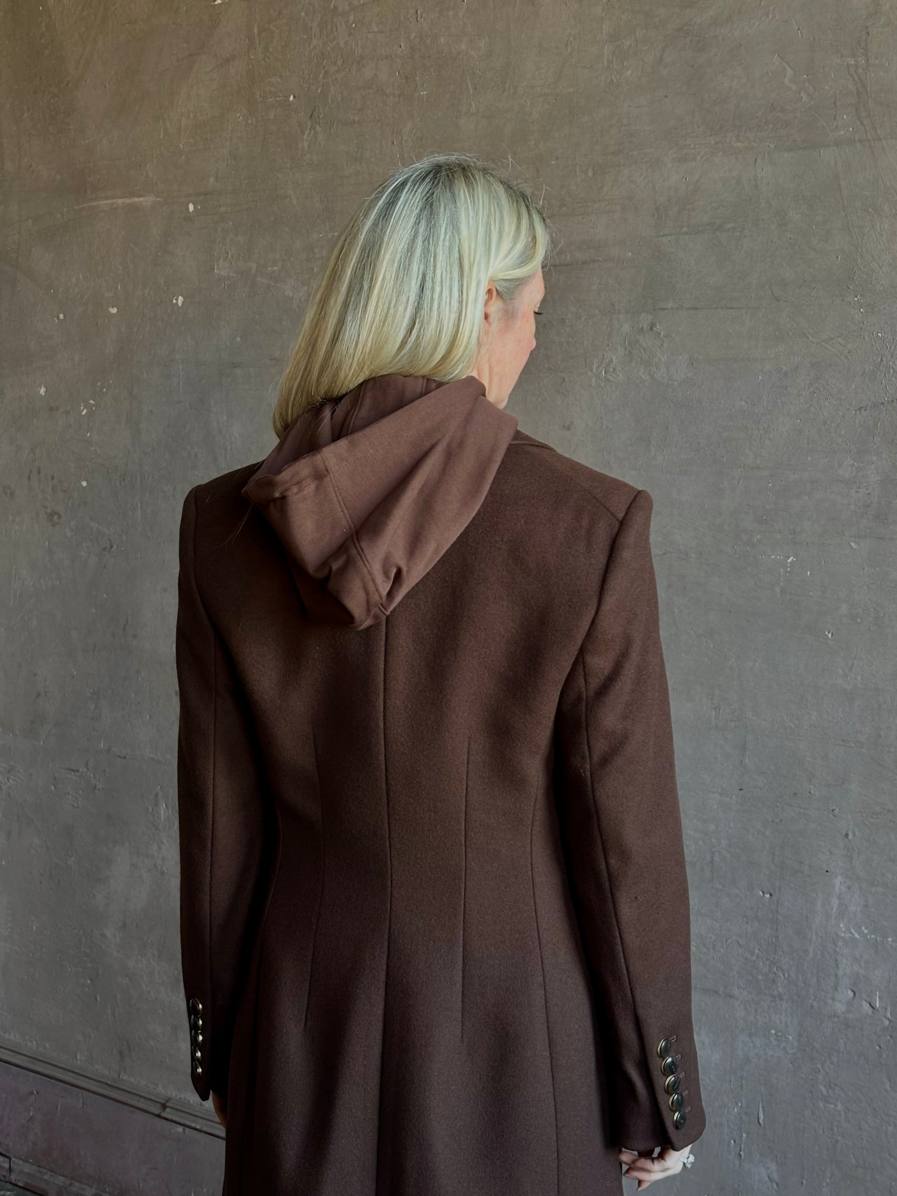 Mature woman wearing Veronica Beard Elspeth Coat with OVS Hoodie Dickey in Espresso brown wool-cashmere A-line coat with a removable hoodie layer. Playful, sculptural cold-weather luxury.