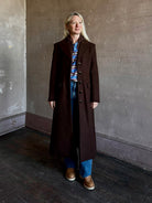 Mature woman wearing Veronica Beard Elspeth Coat with OVS Hoodie Dickey in Espresso brown wool-cashmere A-line coat with a removable hoodie layer. Playful, sculptural cold-weather luxury.
