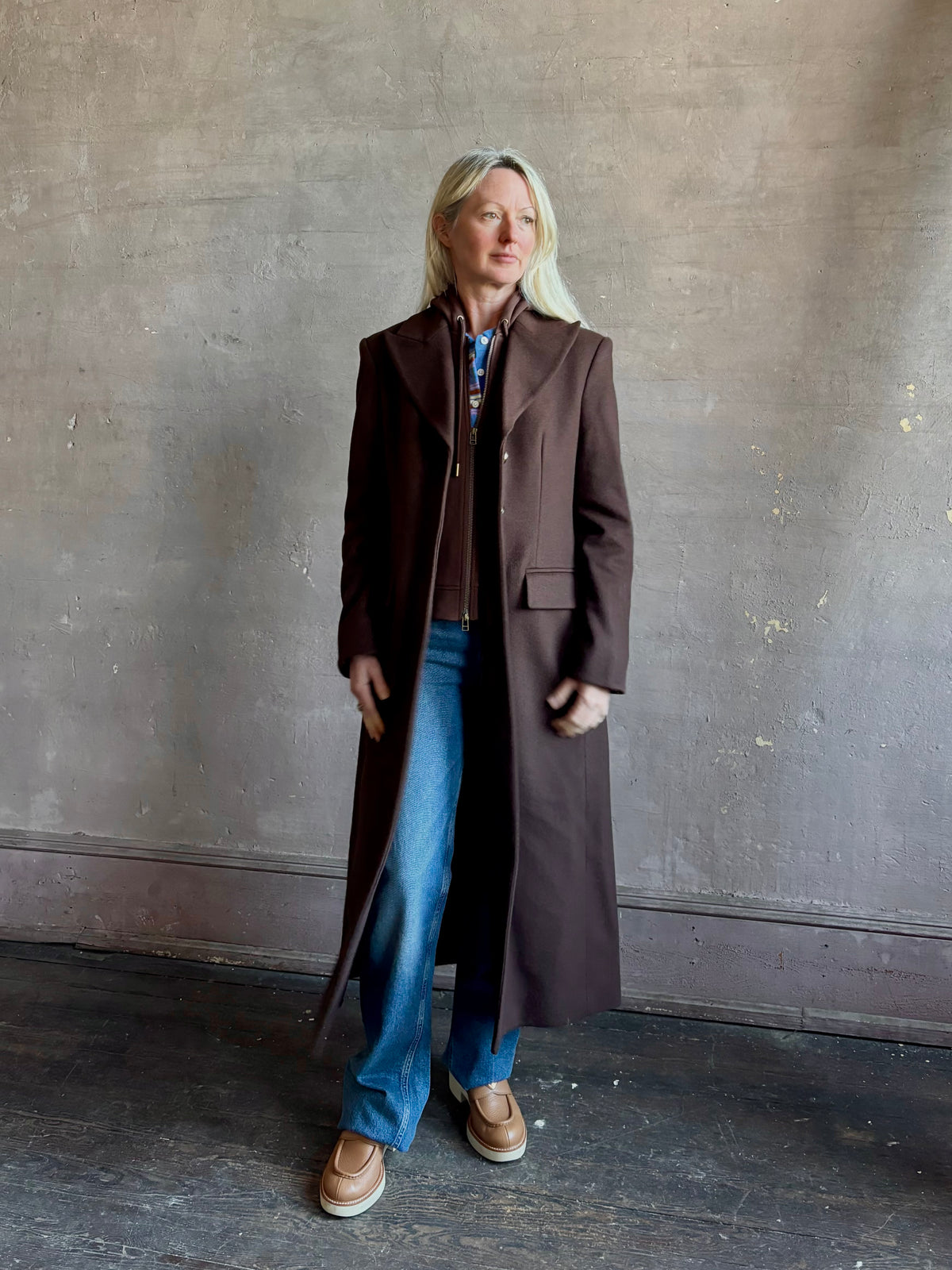 Mature woman wearing Veronica Beard Elspeth Coat with OVS Hoodie Dickey in Espresso brown wool-cashmere A-line coat with a removable hoodie layer. Playful, sculptural cold-weather luxury.