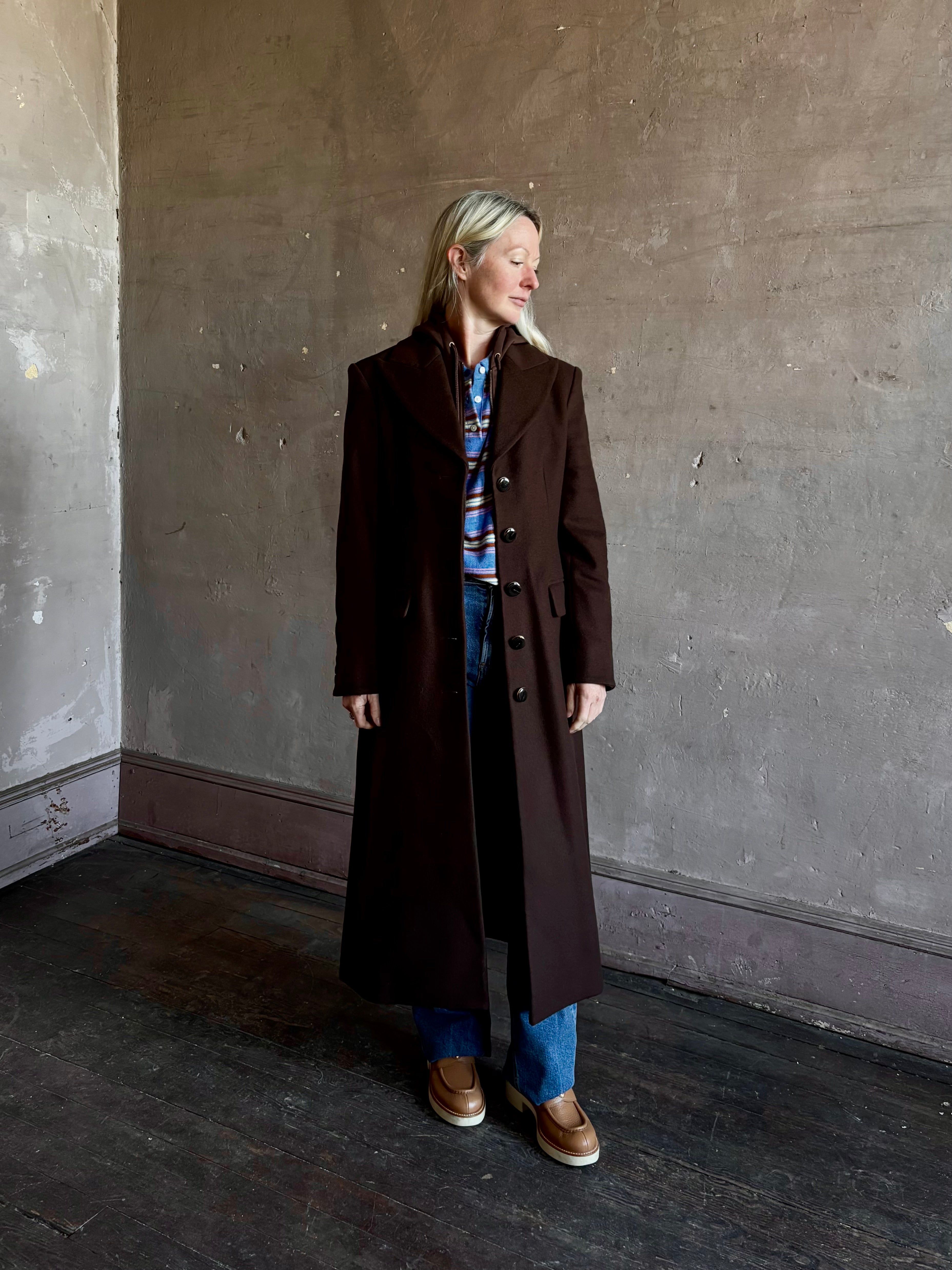 Mature woman wearing Veronica Beard Elspeth Coat with OVS Hoodie Dickey in Espresso brown wool-cashmere A-line coat with a removable hoodie layer. Playful, sculptural cold-weather luxury.
