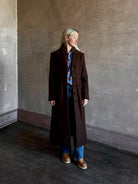 Mature woman wearing Veronica Beard Elspeth Coat with OVS Hoodie Dickey in Espresso brown wool-cashmere A-line coat with a removable hoodie layer. Playful, sculptural cold-weather luxury.