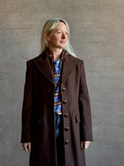 Mature woman wearing Veronica Beard Elspeth Coat with OVS Hoodie Dickey in Espresso brown wool-cashmere A-line coat with a removable hoodie layer. Playful, sculptural cold-weather luxury.