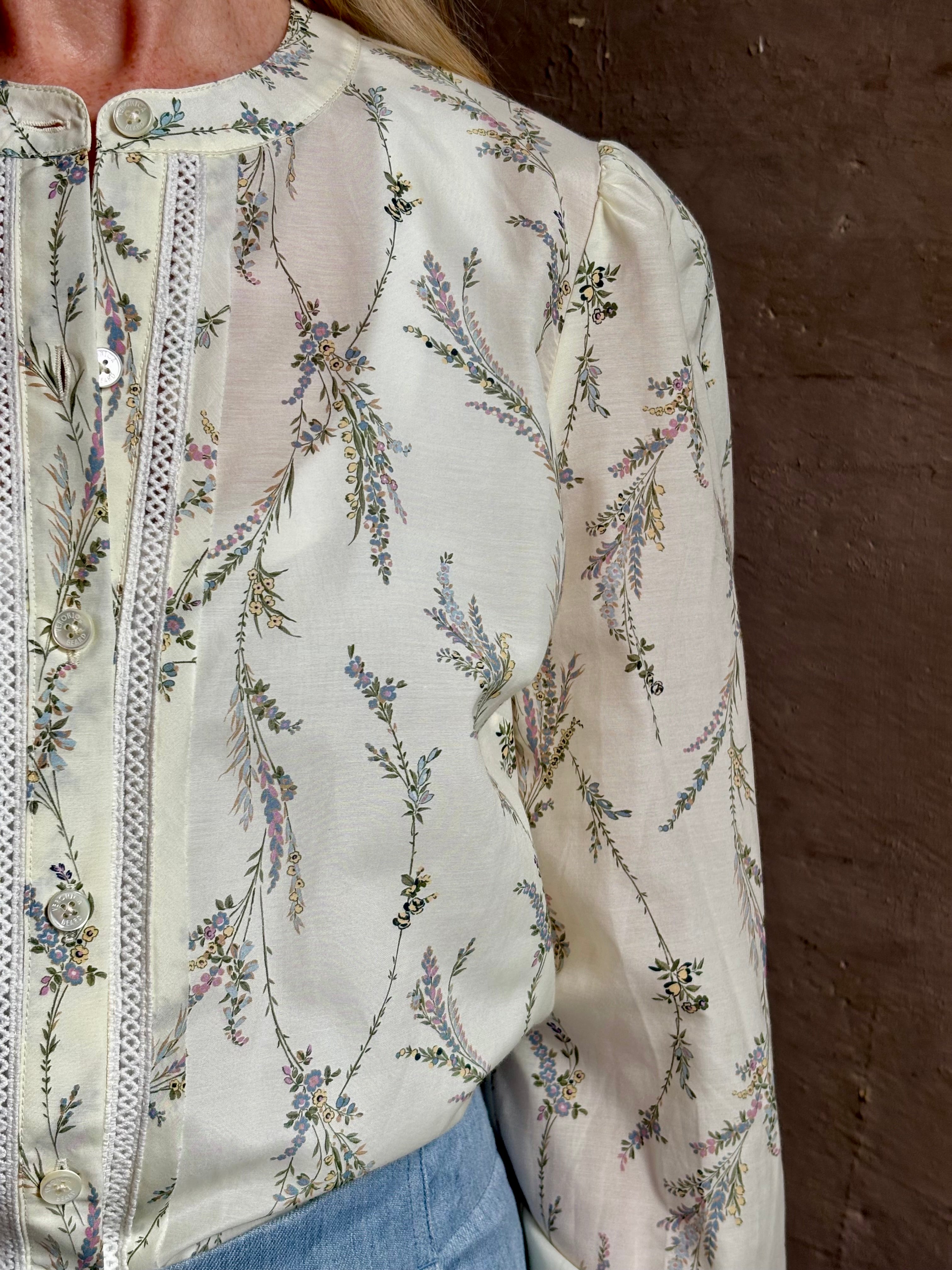 Mature woman wearing luxurious tailored Emiko Blouse from Veronica Beard a women's designer blouse rendered in a cream  ground adorned with a delicate prairie floral print and crafted from a cotton and silk blend with long sleeves, button front and round mandarin collar.