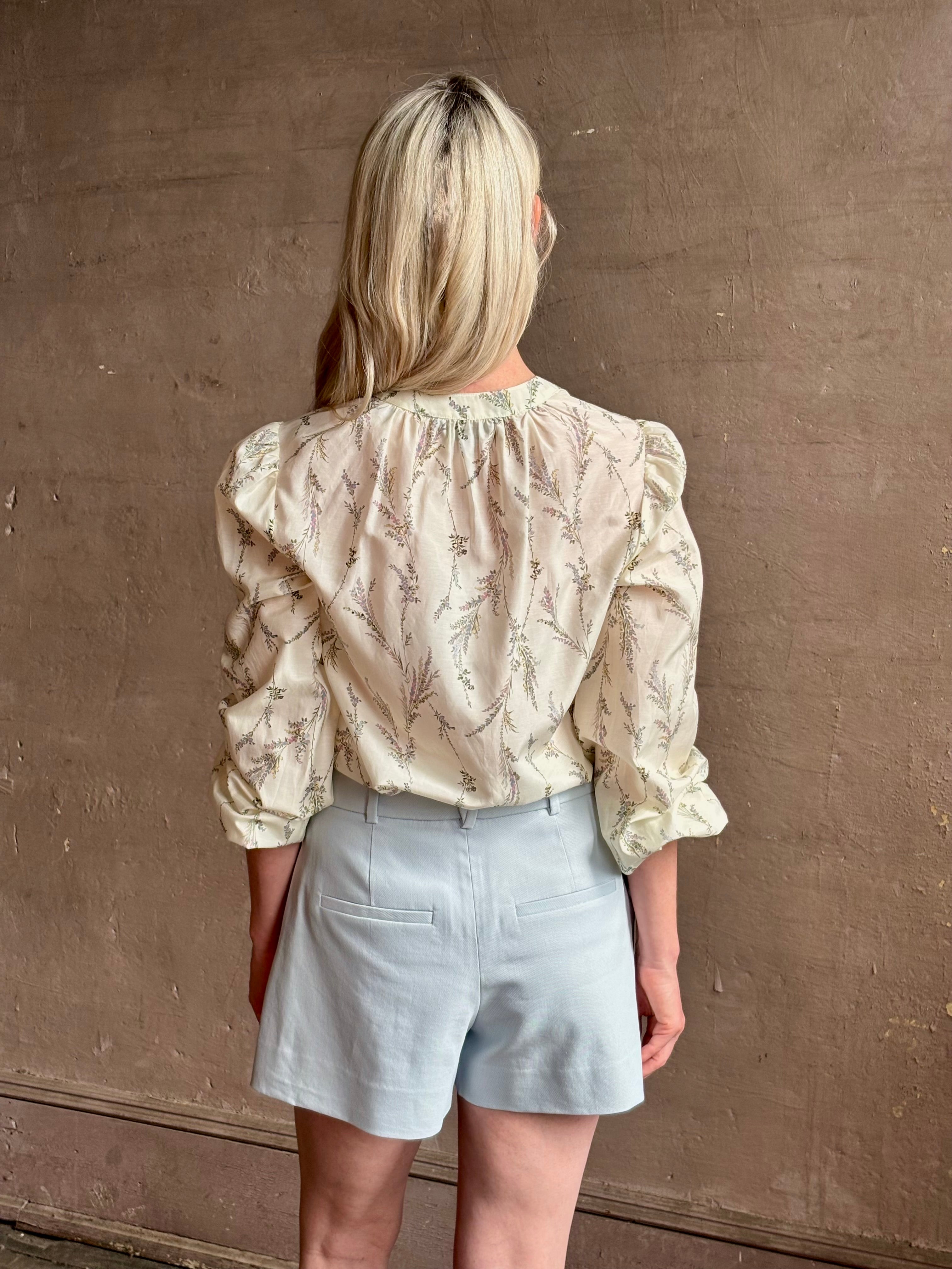 Mature woman wearing luxurious tailored Emiko Blouse from Veronica Beard a women's designer blouse rendered in a cream  ground adorned with a delicate prairie floral print and crafted from a cotton and silk blend with long sleeves, button front and round mandarin collar.