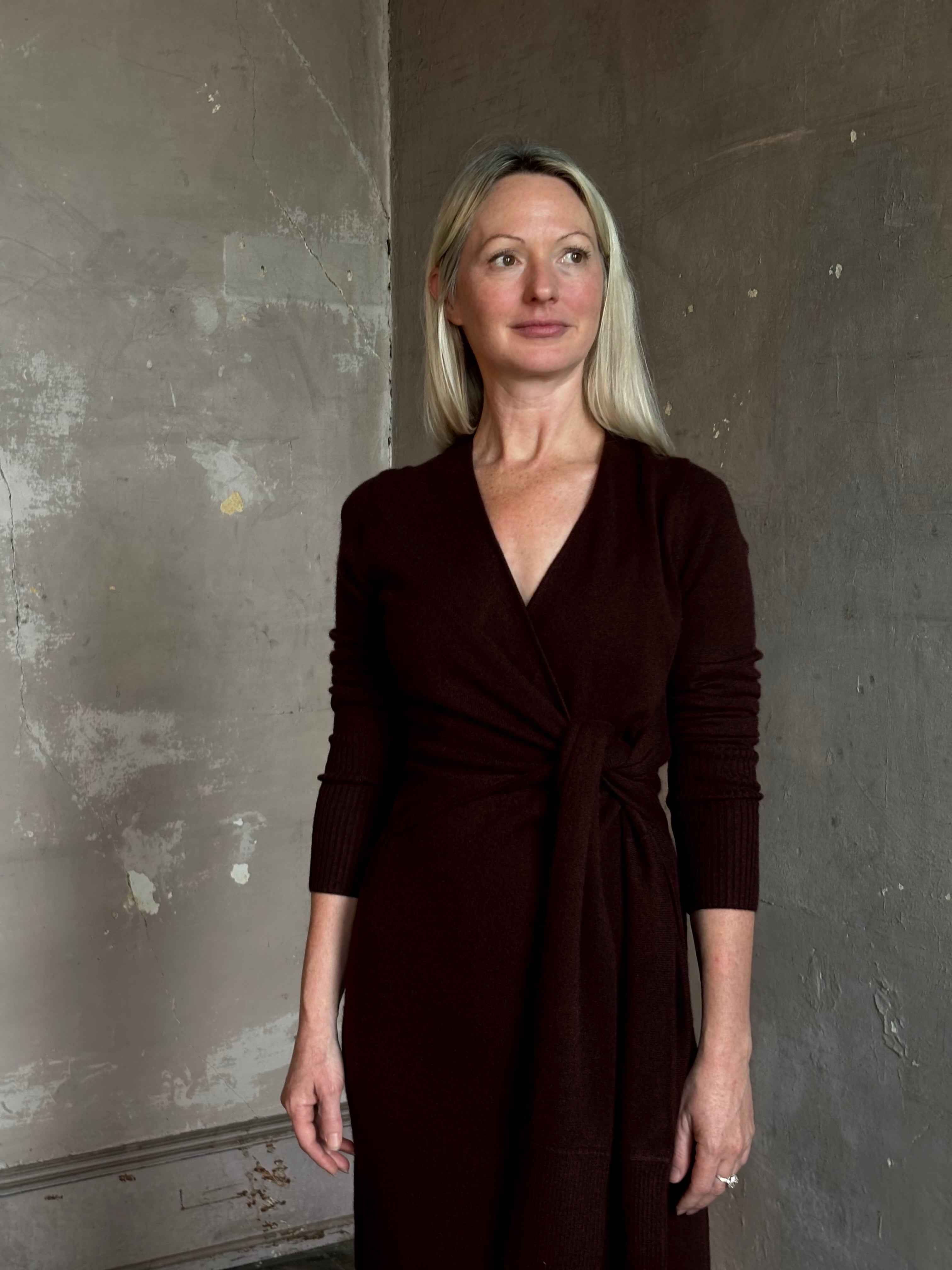 Mature woman wearing Veronica Beard's Salomez Knit Dress in chocolate brown  wrap maxi with a V-neckline and side vent