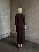 Mature woman wearing Veronica Beard's Salomez Knit Dress in chocolate brown  wrap maxi with a V-neckline and side vent
