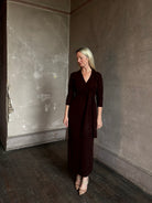 Mature woman wearing Veronica Beard's Salomez Knit Dress in chocolate brown  wrap maxi with a V-neckline and side vent