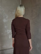 Mature woman wearing Veronica Beard's Salomez Knit Dress in chocolate brown  wrap maxi with a V-neckline and side vent