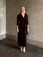 Mature woman wearing Veronica Beard's Salomez Knit Dress in chocolate brown  wrap maxi with a V-neckline and side vent