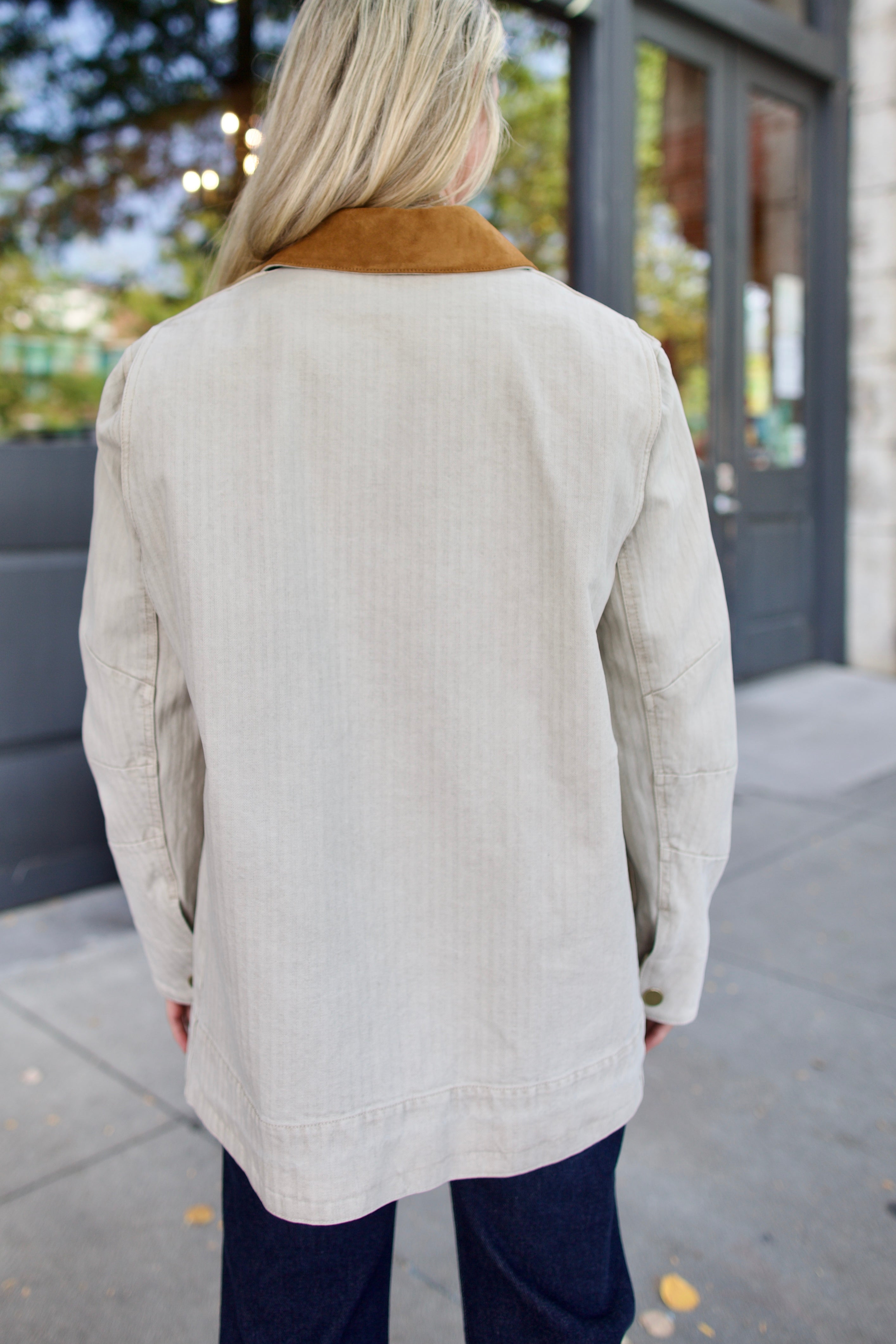 Back of model wearing an elevated casual light weight barn jacket with a suede collar and denim.