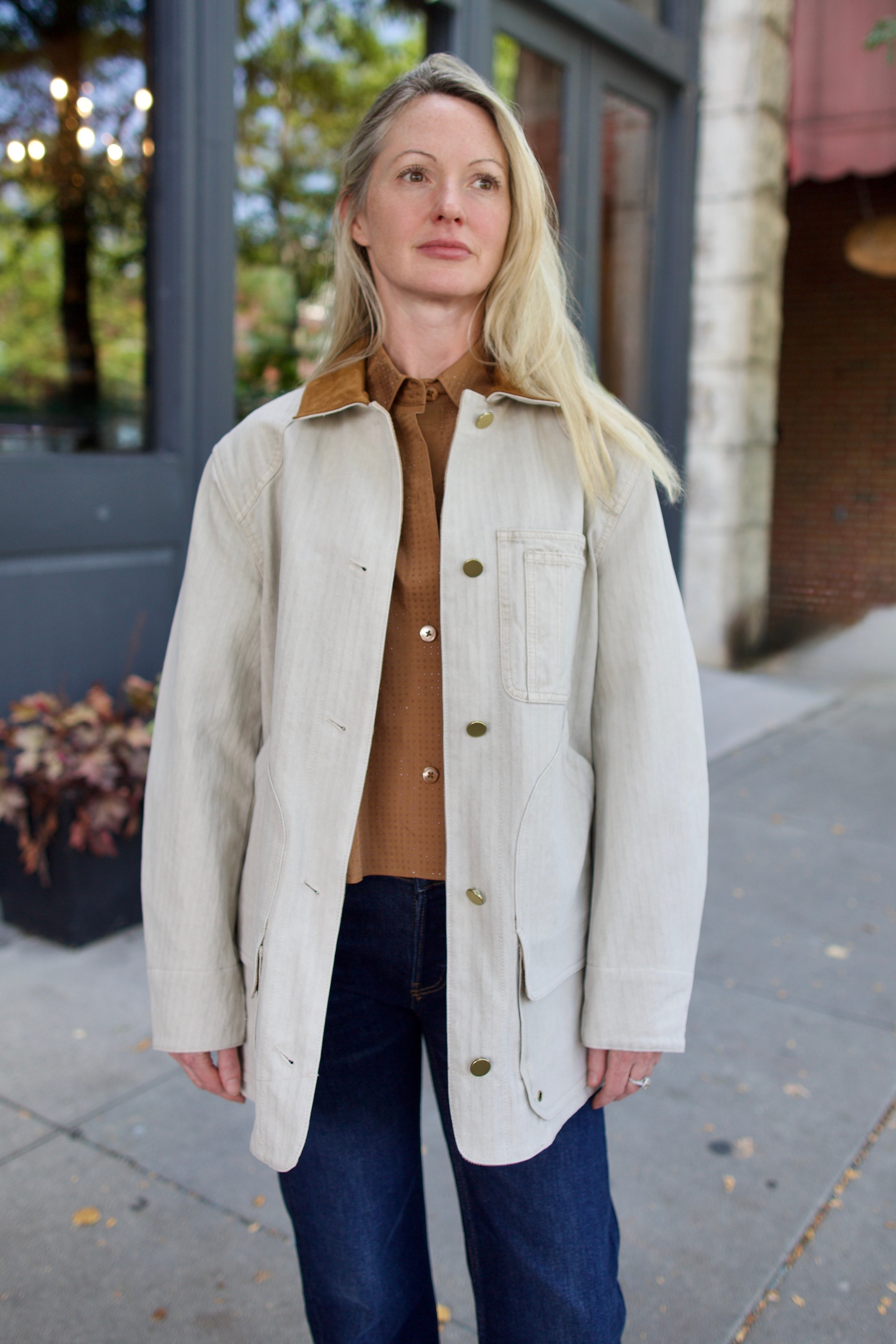 Model wearing a light weight cotton beige barn jacket from Veronica Beard over a TWP brown shirt with blue denim.