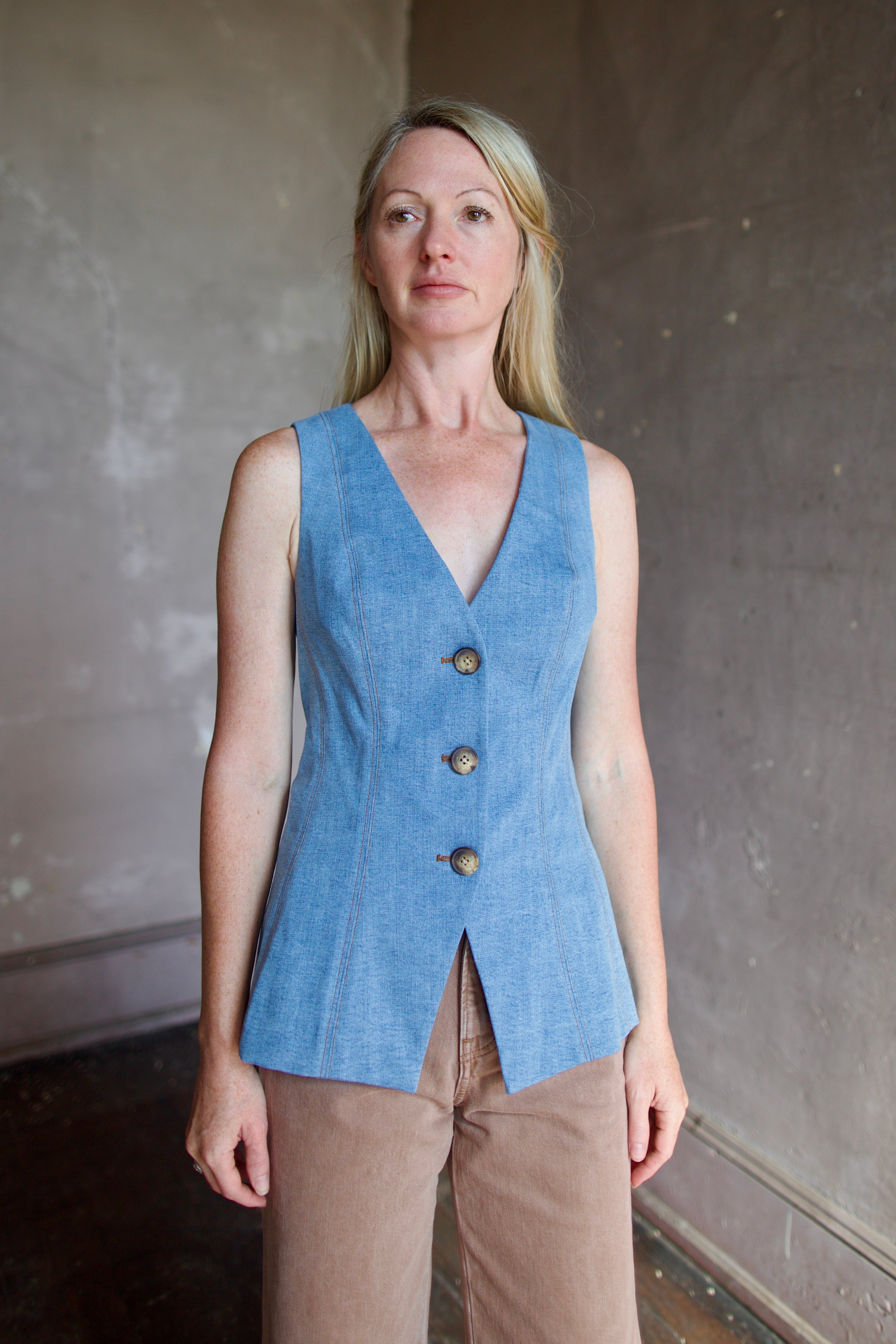 Model wearing designer Veronica Beard Avalina Vest in Blue Mirage with v-neck sleeveless design and contrasting  brown thread seaming