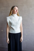 Image featuring a woman wearing the Holton Knit Vest by Veronica Beard with a mock neck, button detailing down left shoulder and intricate knit wool detailing in cream.