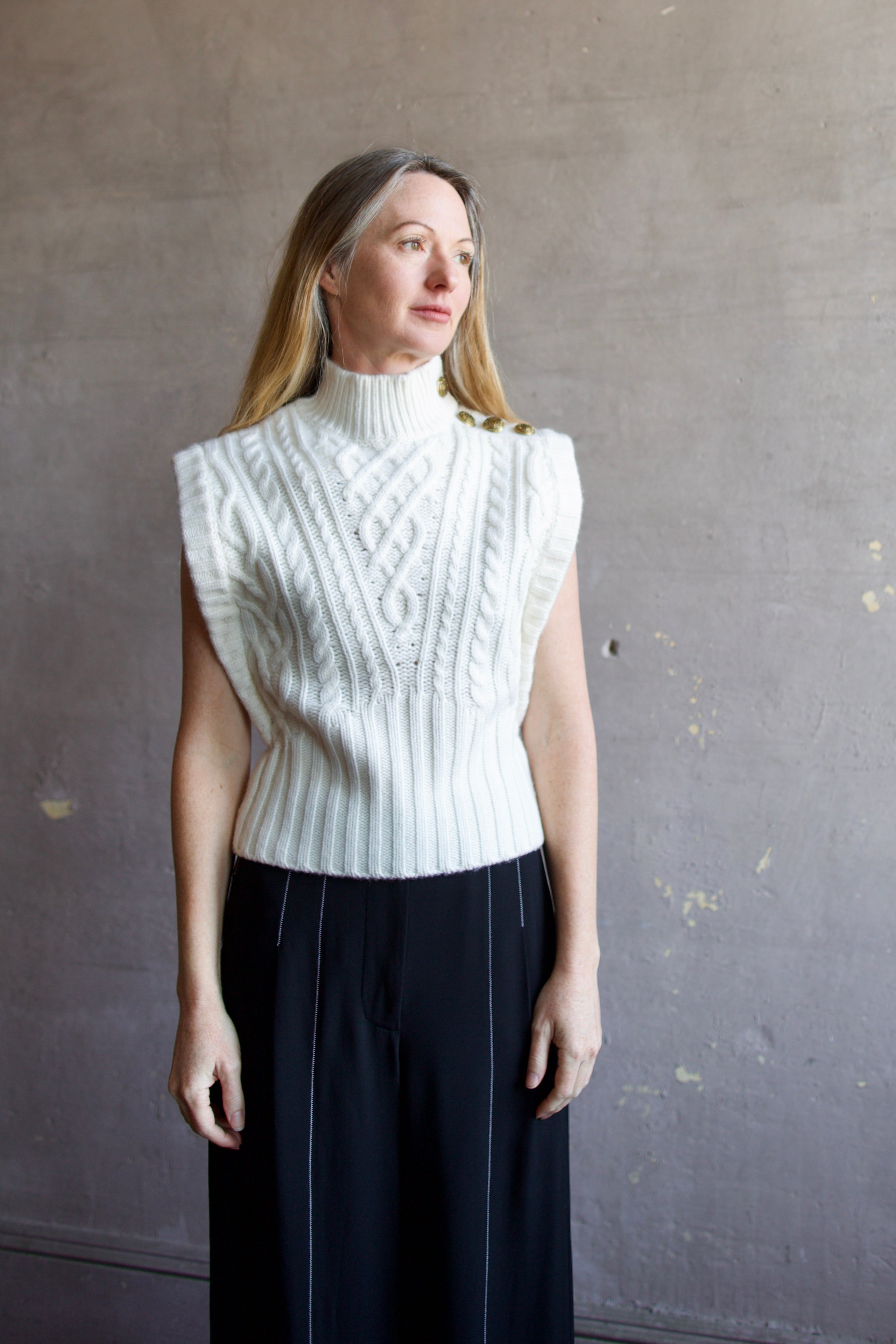 Image featuring a woman wearing the Holton Knit Vest by Veronica Beard with a mock neck, button detailing down left shoulder and intricate knit wool detailing in cream.