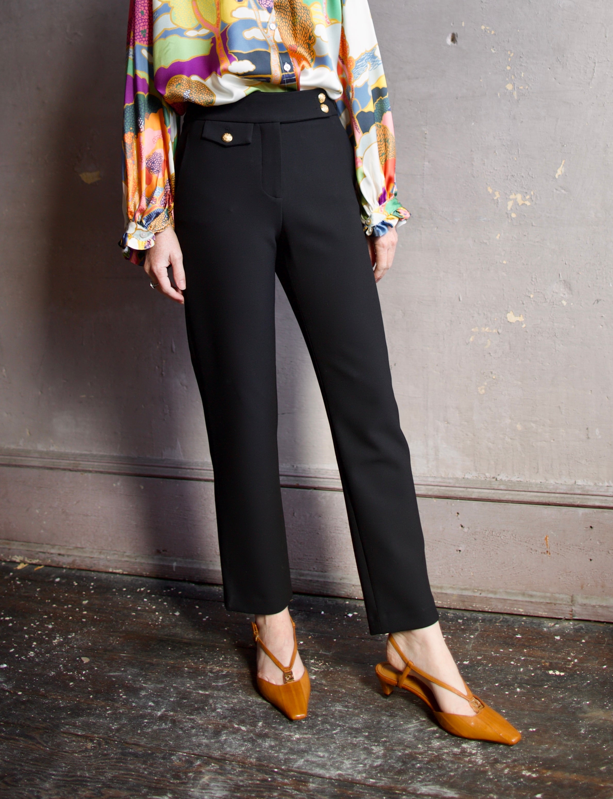 Image featuring a woman wearing the Renzo Pants by Veronica Beard with a tab waistband with a mid rise and straight leg in black with gold finish buttons.