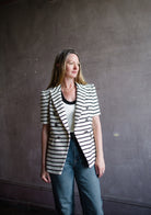 Image featuring a woman wearing the Jenny jacket by Veronica Beard with short sleeves and a tailored fit. The black stripe has a slight metallic sheen on ivory.