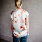 Image featuring a woman wearing the Vince poppy silk blouse with a band collar, split neckline, and short dolman sleeves, and showcases an abstract blurred poppy print.