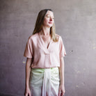 Image featuring a woman wearing a silk blend blouse by Vince with a split neckline with short sleeves and a relaxed fit in blush colorway.