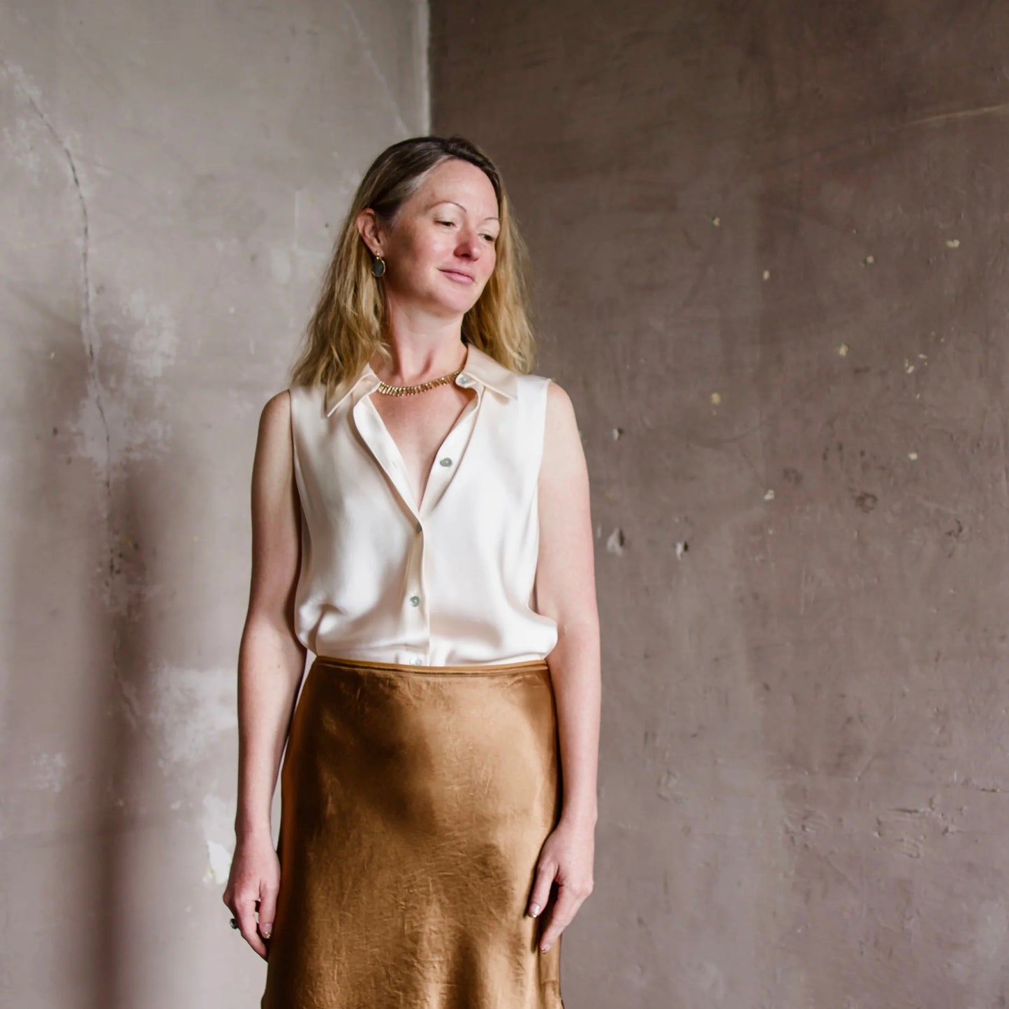 Image featuring a woman wearing a Vince Sleeveless Silk Blouse in cream and styled with a classic copper skirt.