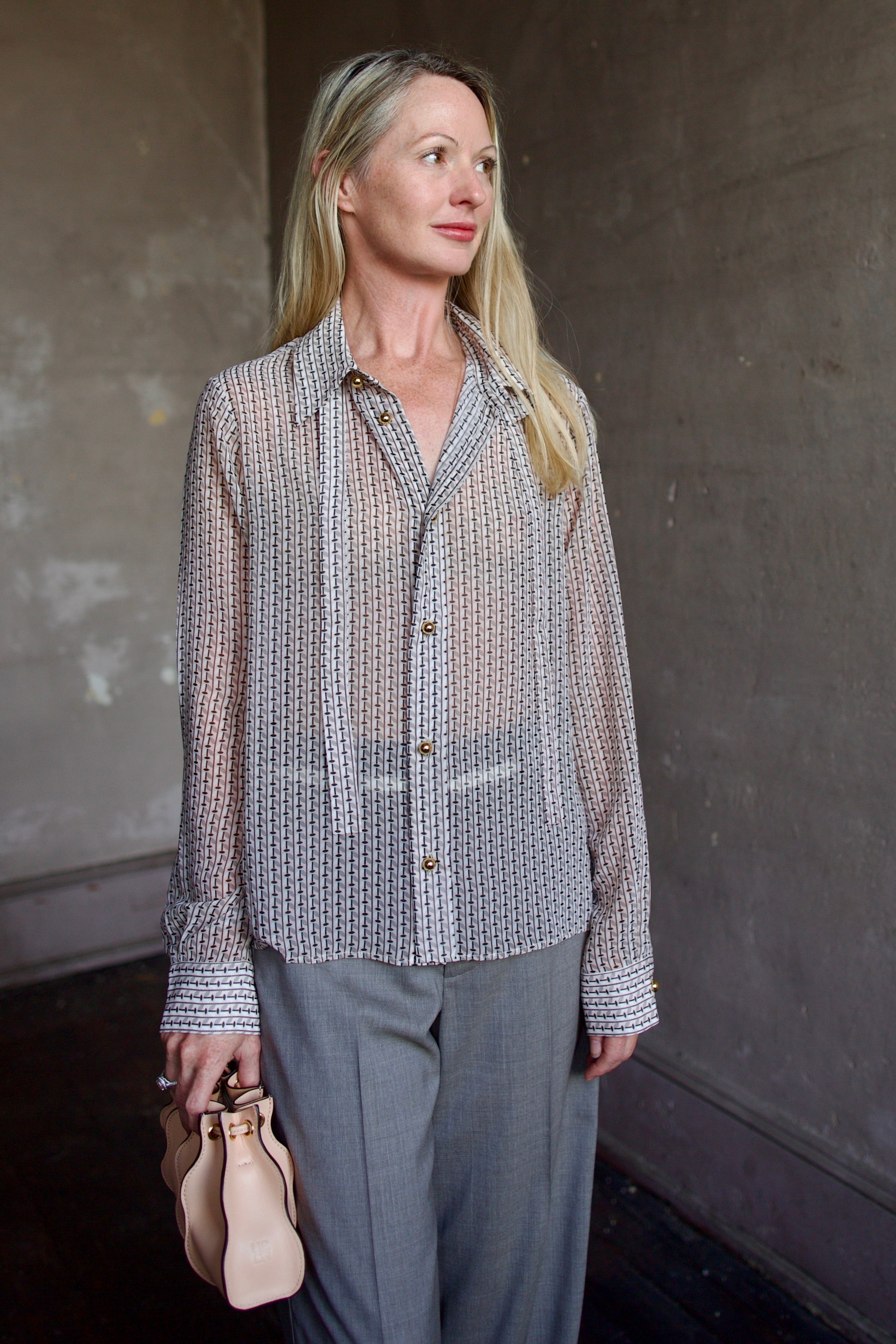 Mature model wearing a sheer geometric shirt with round gold metal buttons by designer WE-AR4