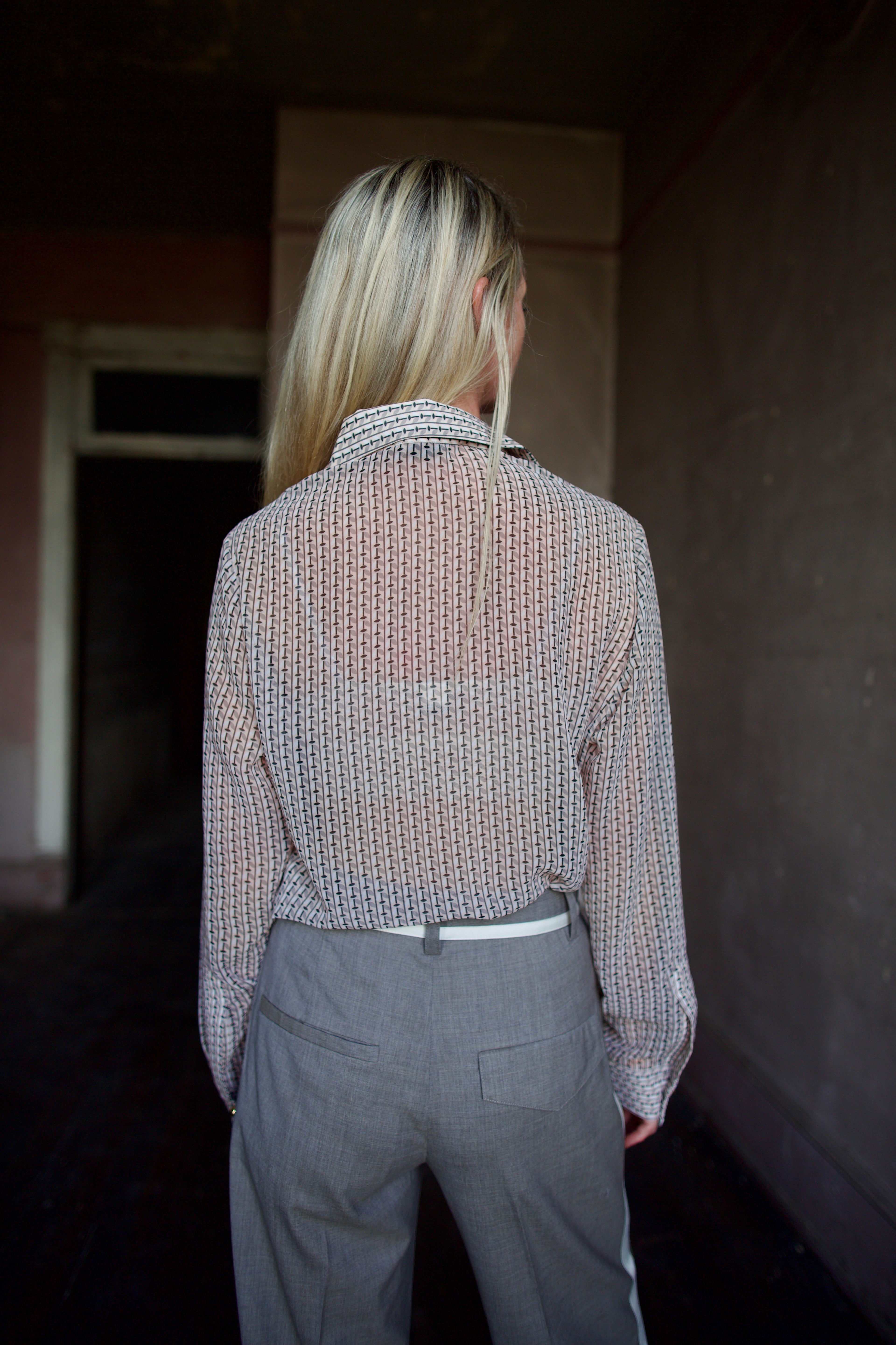 Mature model wearing a sheer geometric shirt with round gold metal buttons by designer WE-AR4