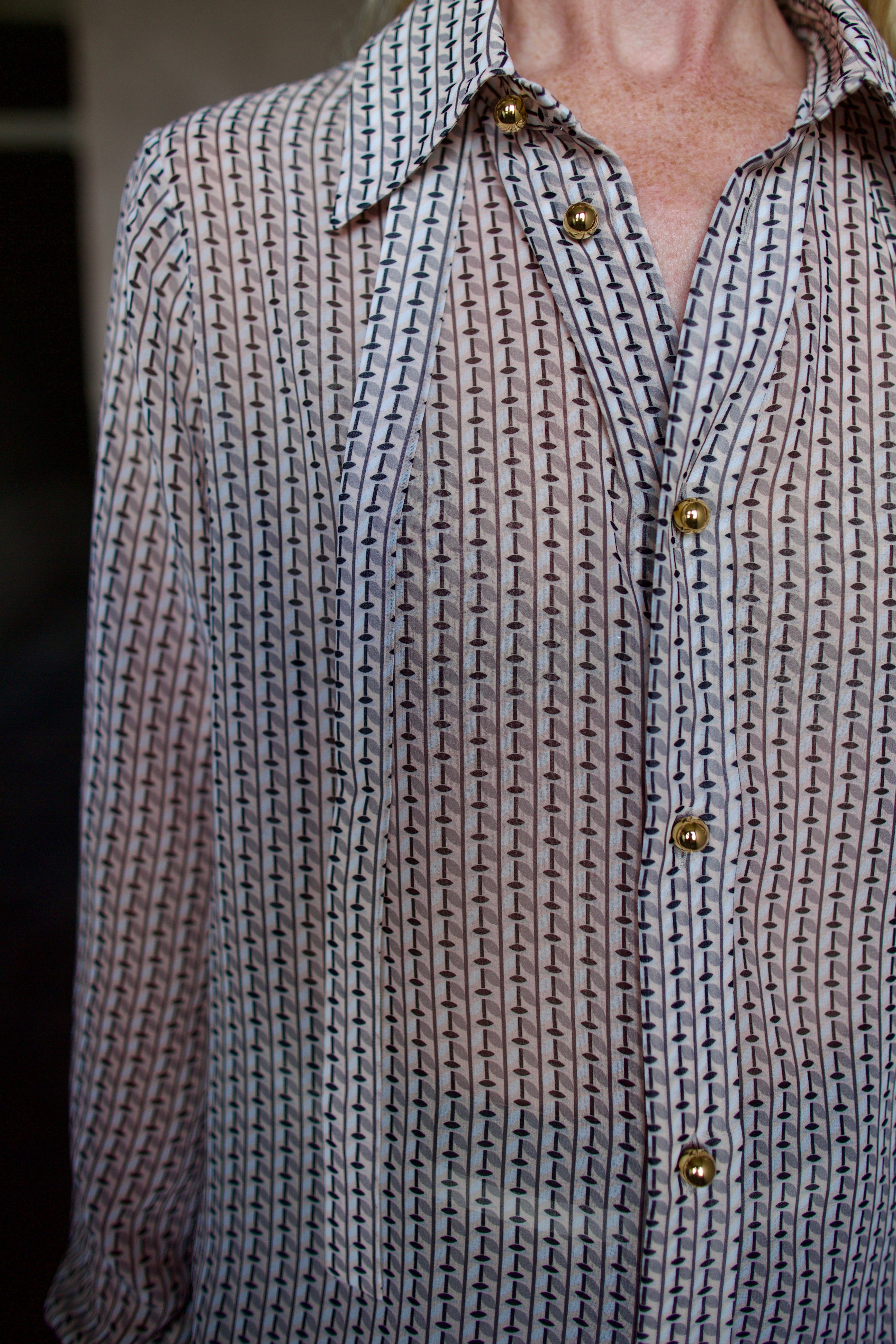 Mature model wearing a sheer geometric shirt with round gold metal buttons by designer WE-AR4