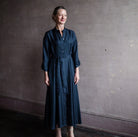 Image featuring a woman wearing the Xirena Sabine shirt dress in navy button down with a full midi-length skirt and rounded collar.