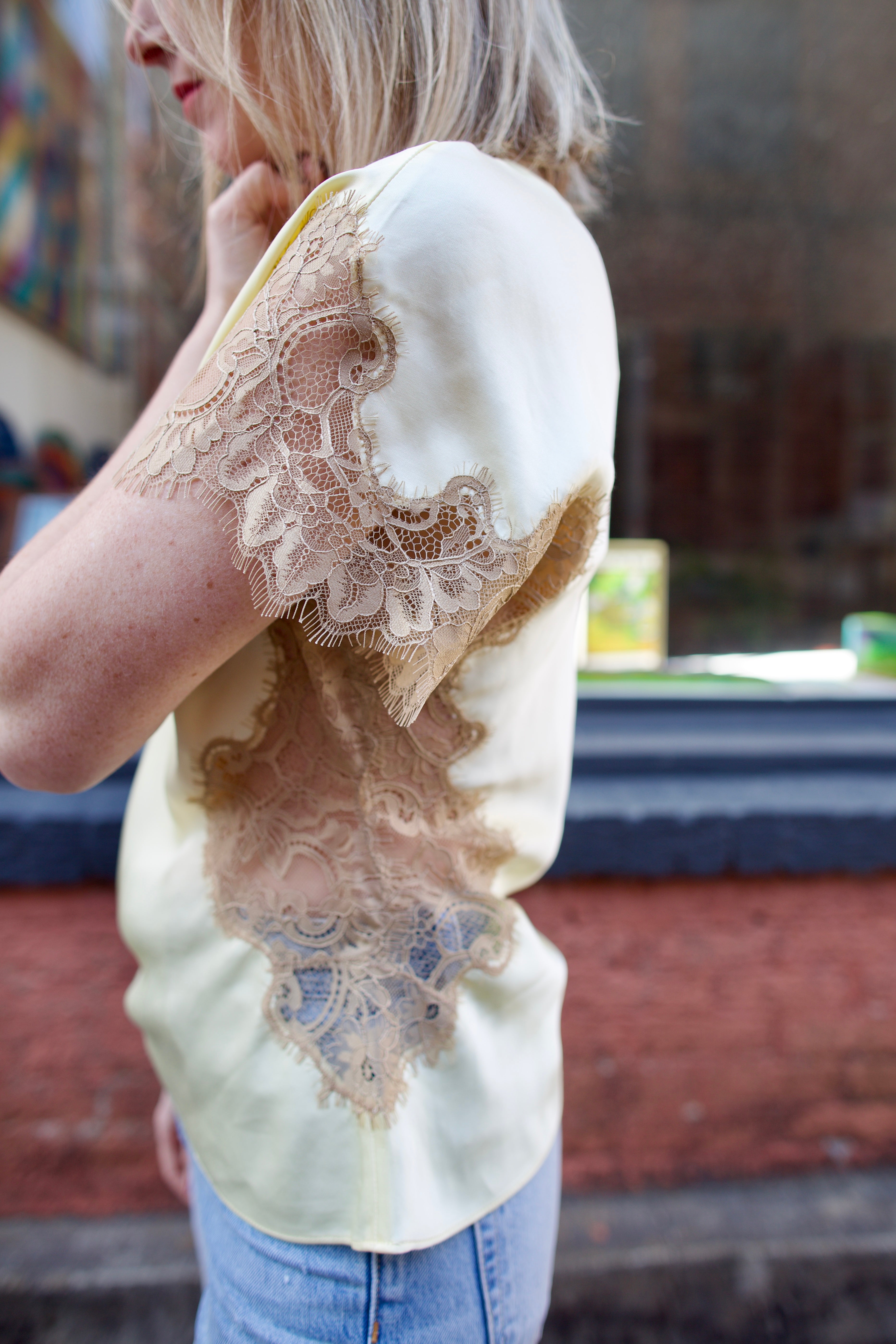 Mature woman wearing the yellow and beige ALC Alessia Top with open neckline, asymmetrical fit and lace detailing